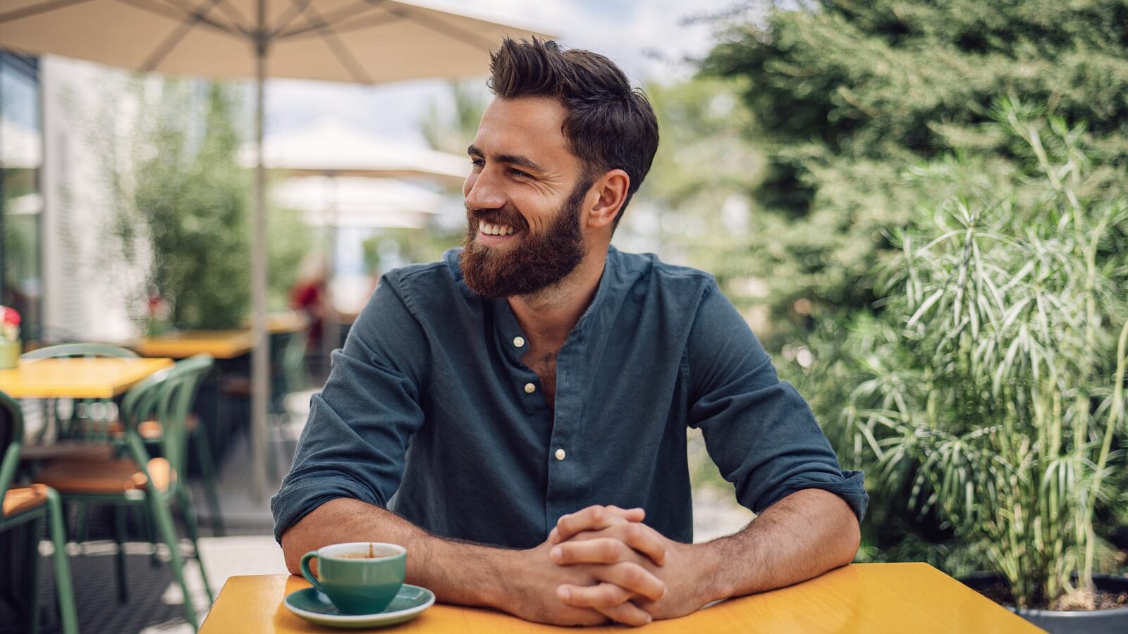 Smiling man with a full, neatly shaped beard at an outdoor cafe table