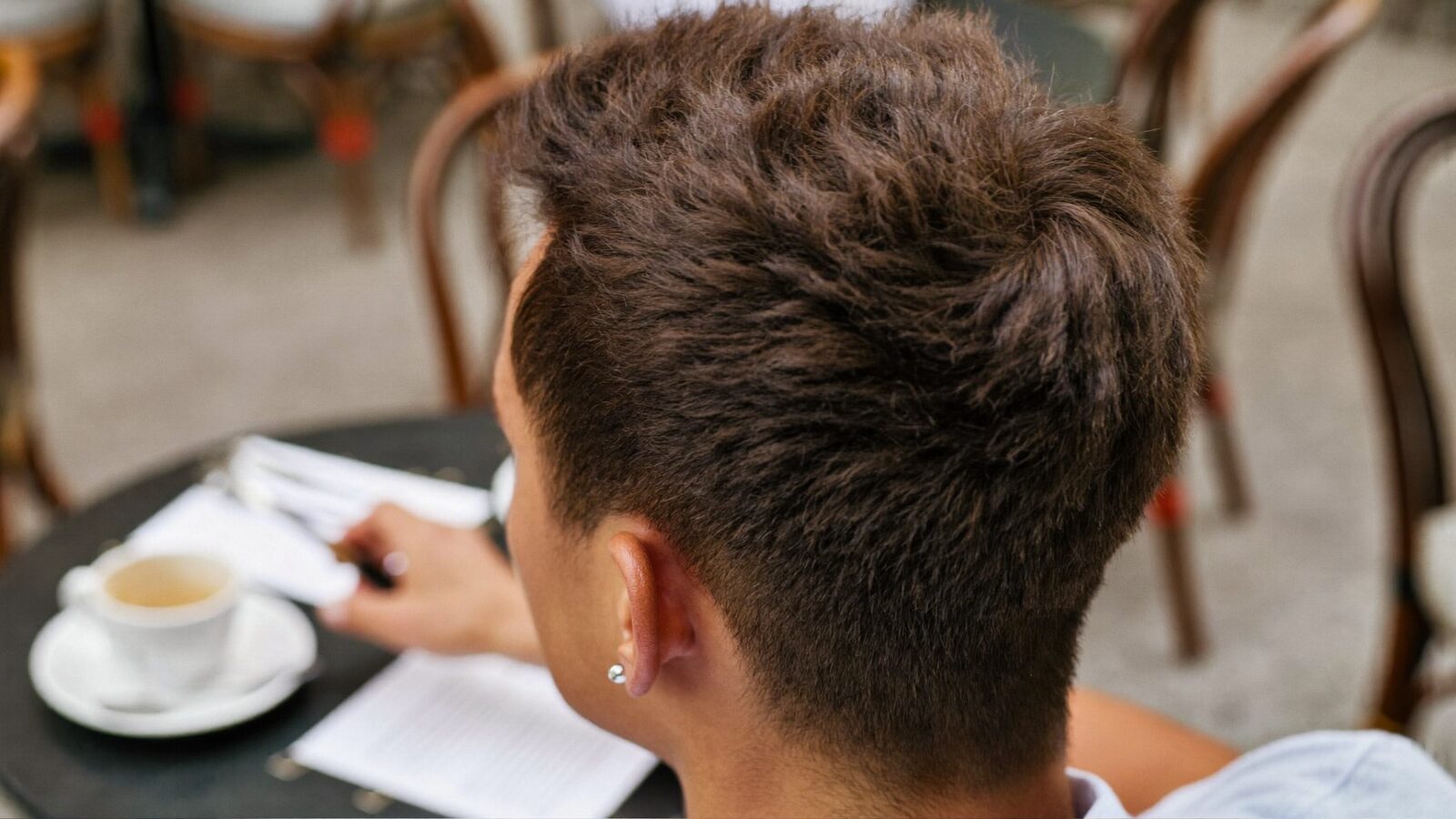 Back of a man's head showing a full, dense crown of short brown hair at an outdoor cafe