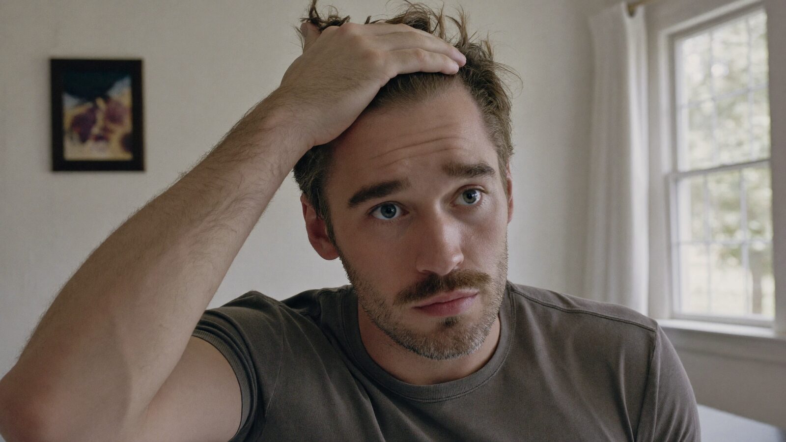 Man running a hand through his hair at the temple in a bright room