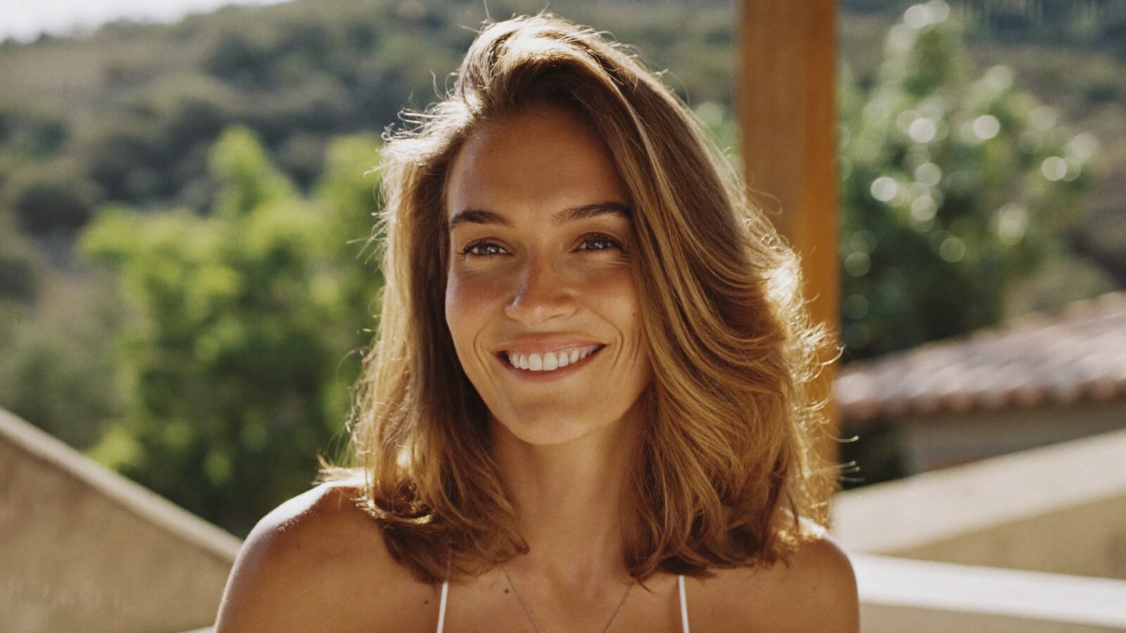 Smiling woman with thick, healthy shoulder-length hair on a sunlit terrace