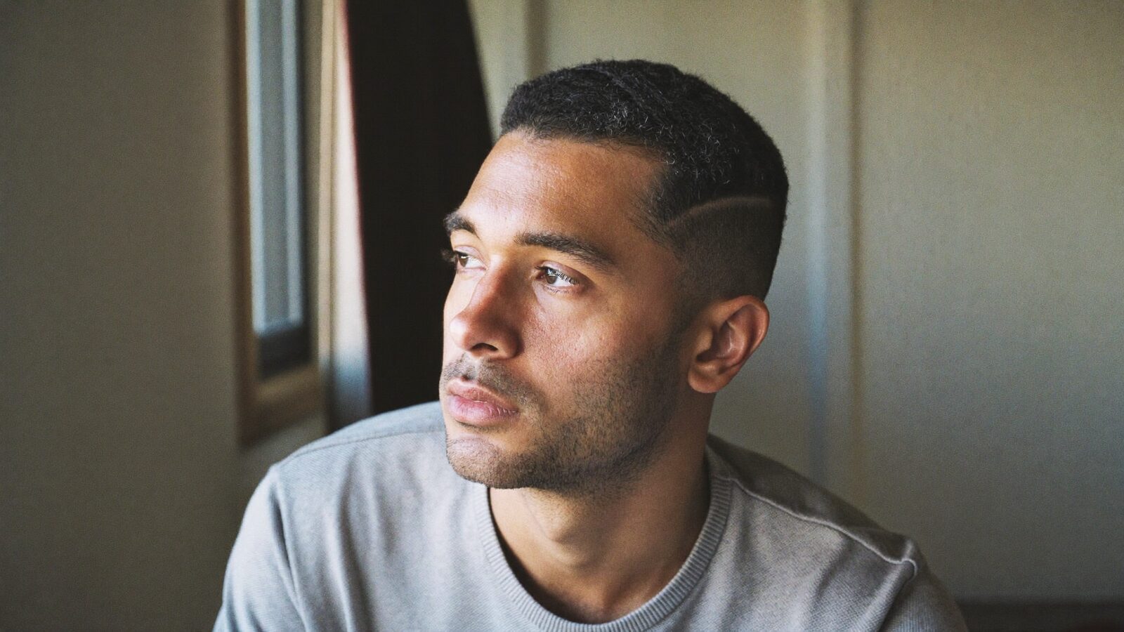Man with a short haircut looking thoughtfully out of a window in soft light