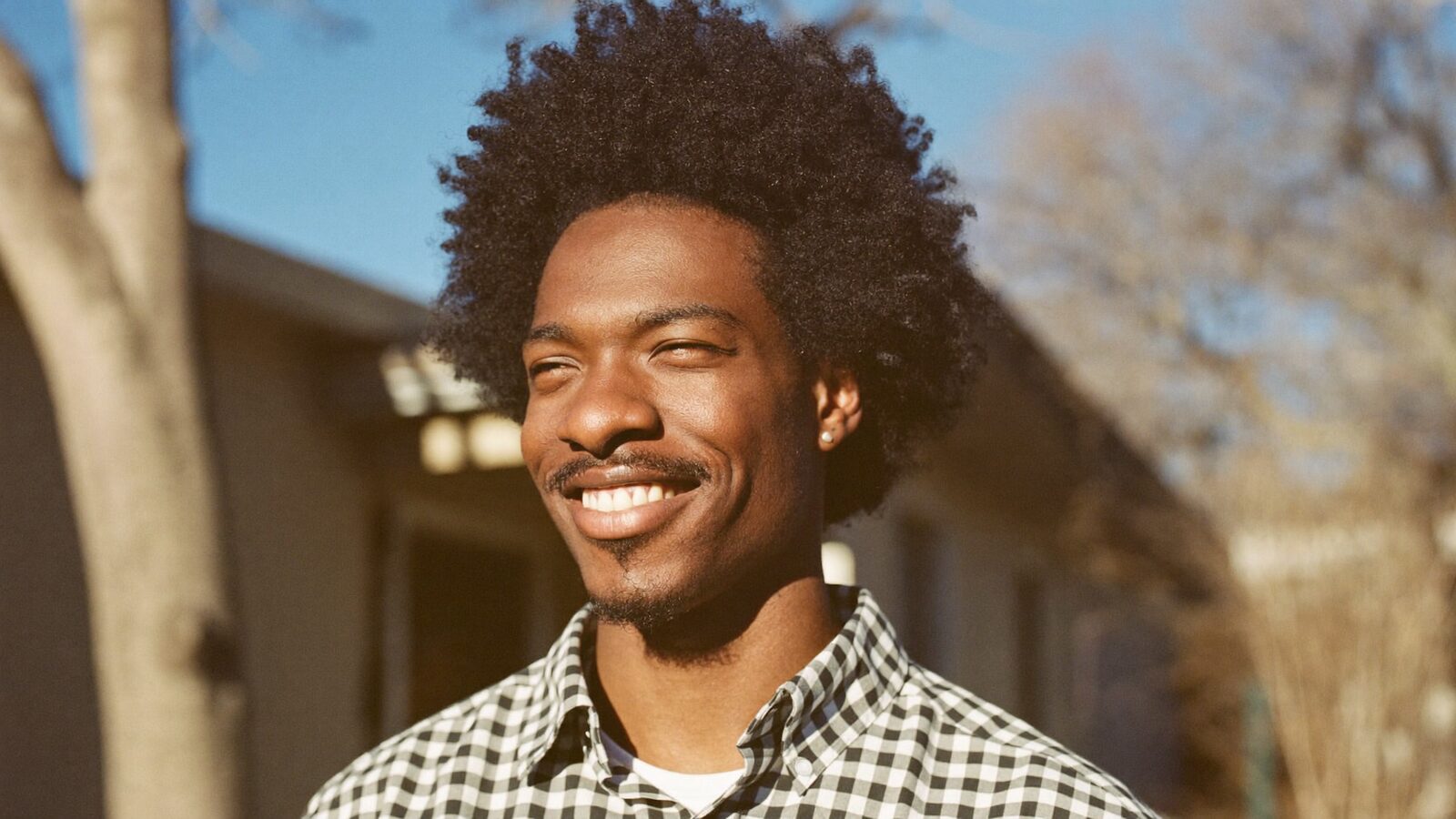 Smiling man with a full, healthy curly hairline outdoors in warm sunlight