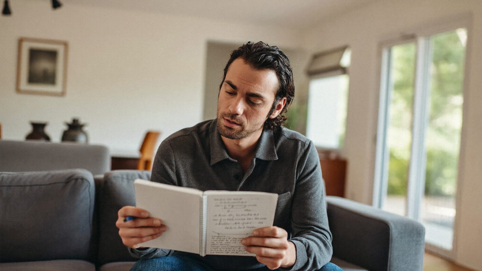 Man with full dark hair reading his notes on a living room sofa