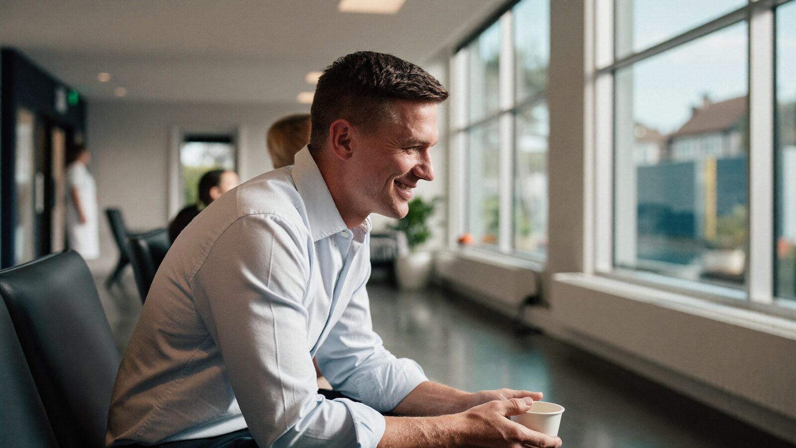 Smiling man with short neat hair holding a cup of tea in a bright clinic waiting area