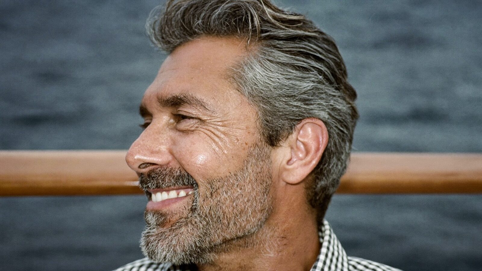 Smiling man with full salt-and-pepper hair on a boat with the sea behind him