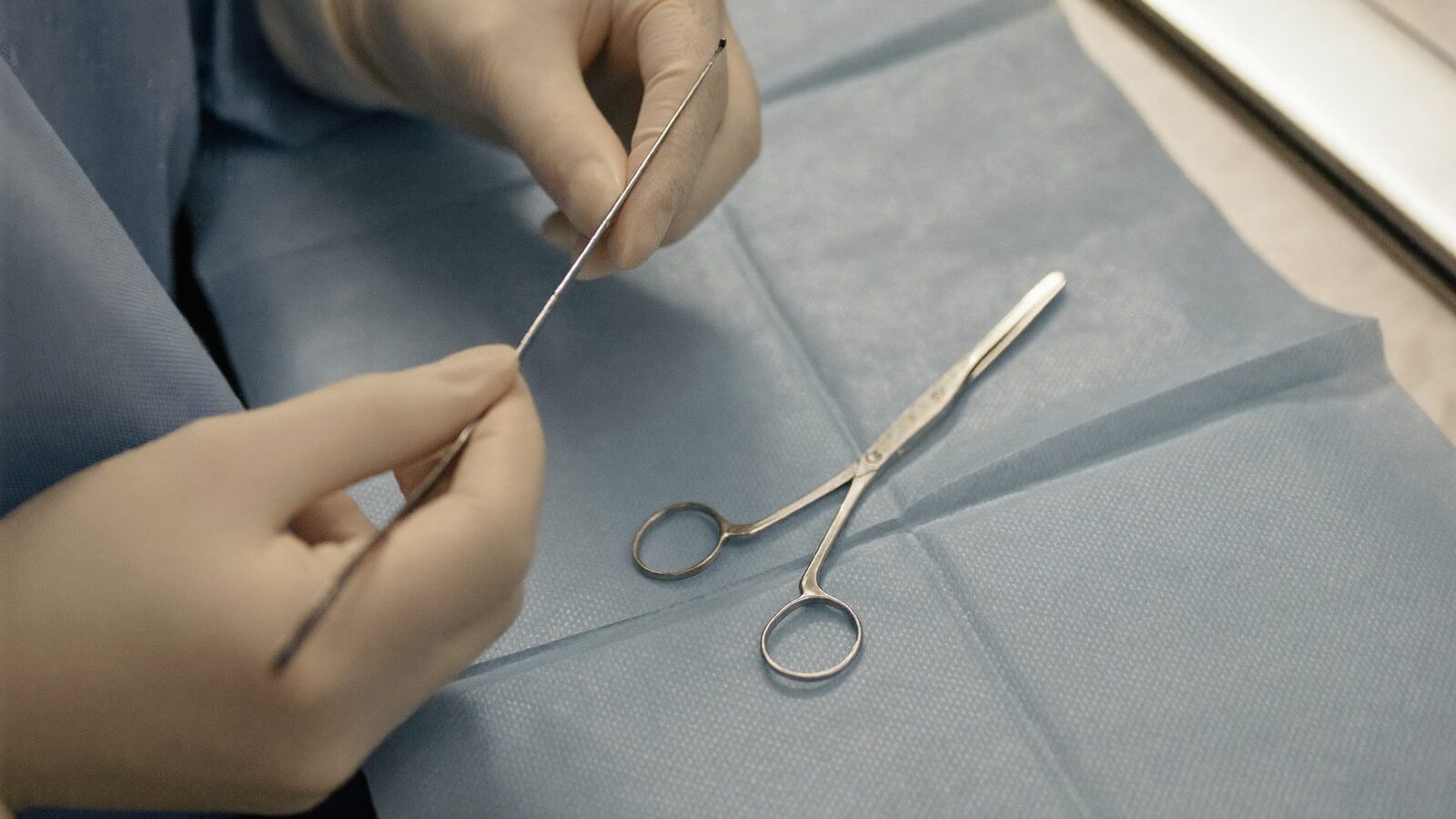 Gloved hands holding a fine handheld surgical instrument over a sterile blue drape