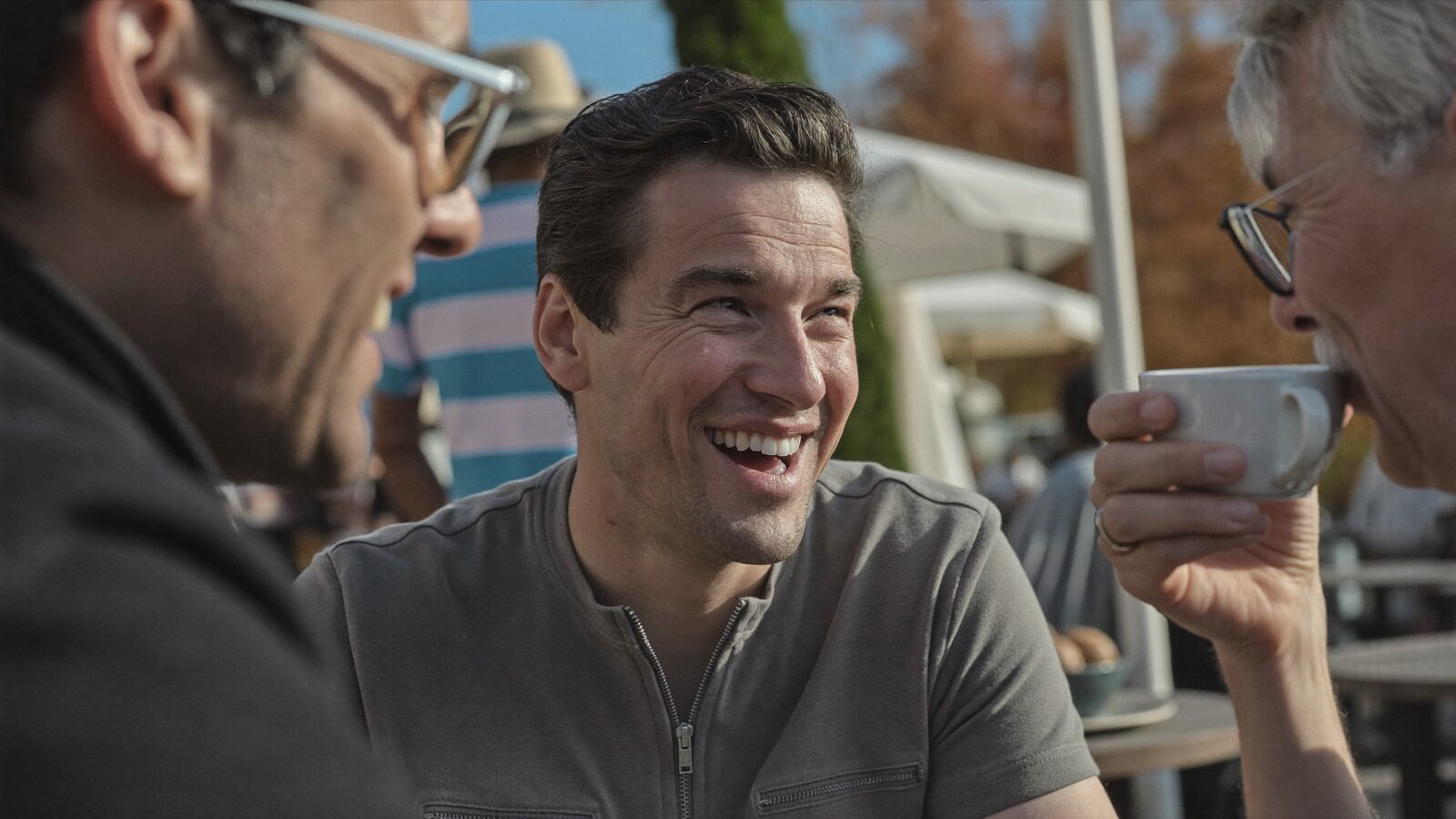 Smiling man with a full, natural-looking hairline at an outdoor cafe with friends